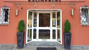 The entrance to Kronprinzt hotel with a glass door, two potted plants, and a sign above the door. - Hotel Kronprinz (Minden)