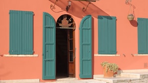 Un edificio con dos contraventanas verdes abiertas, una puerta de madera y una cesta colgante con flores.