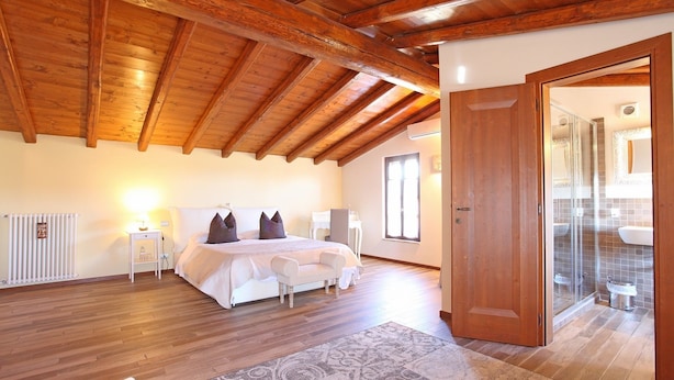 Un dormitorio con techo de madera, una cama con ropa de cama blanca, una mesita de noche con lámpara y un baño con cabina de ducha de vidrio.