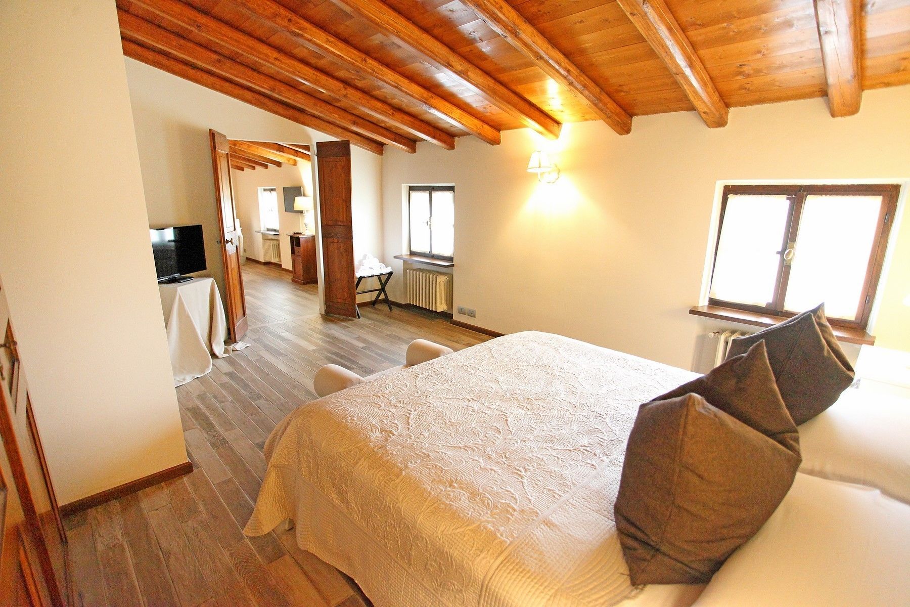 Un dormitorio con cama, vigas de madera en el techo, una ventana y un televisor en la habitación contigua.