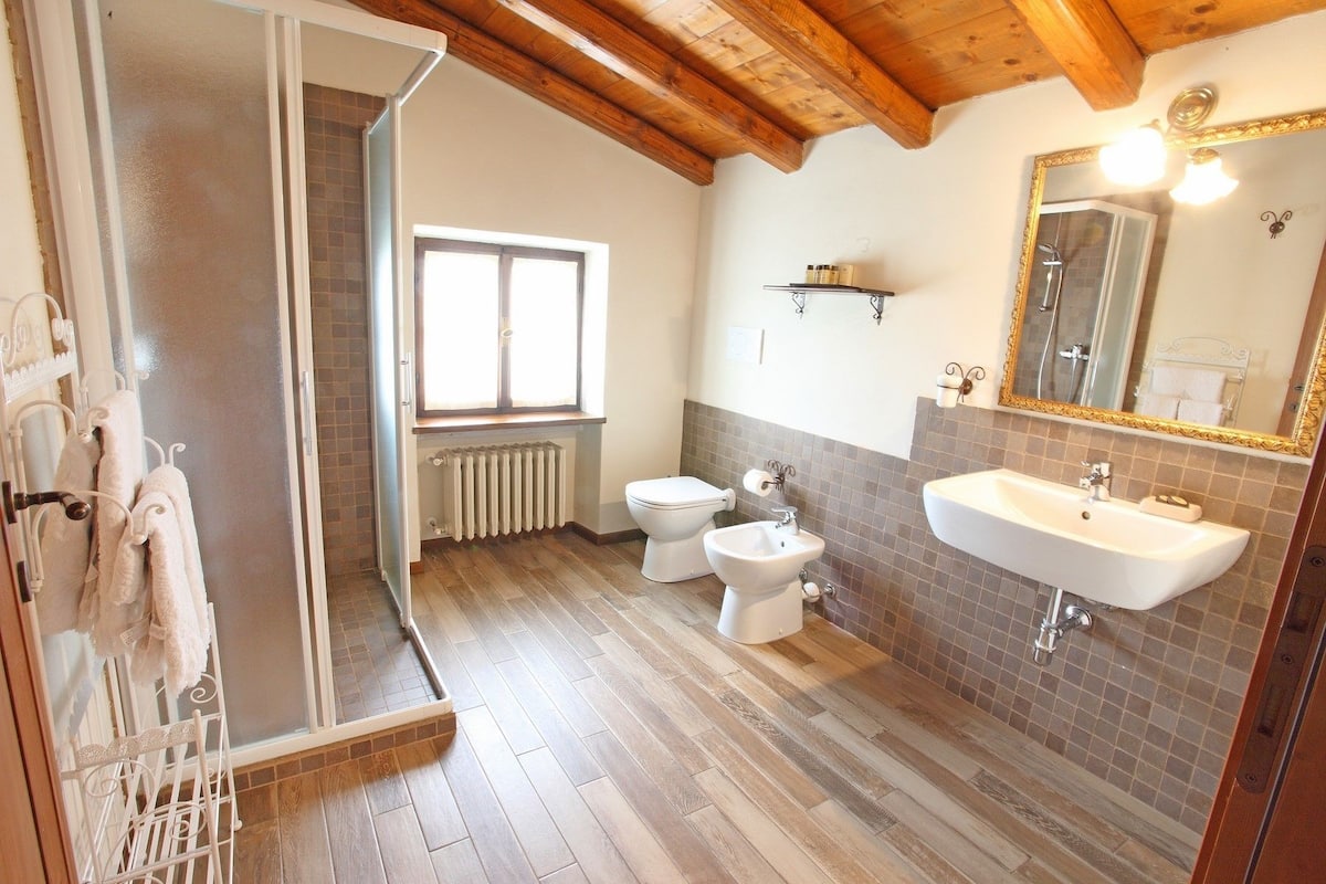 Een badkamer met een houten vloer, een radiator, toilet, bidet, wastafel en een spiegel met gouden lijst.