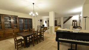 Amplia sala de estar con comedor, un piano y una escalera que sube a otro nivel.