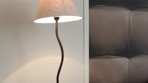 Een houten bijzettafeltje met een lamp, een bekleed hoofdbord en een witte structuurwand.