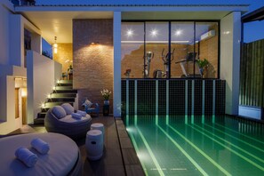 A modern indoor swimming pool area with a brick wall, exercise equipment, and a seating area with cushions. - Chala Number 2 Art and Gallery House (Chiang Mai)