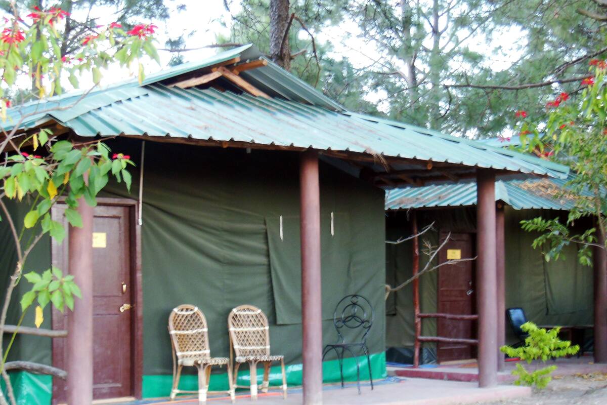 A small, rustic building with a green roof and a covered porch. There are two wicker chairs on the porch.