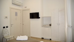 Una habitación de hotel con cama, una silla, televisor, armario y una pequeña cocina.