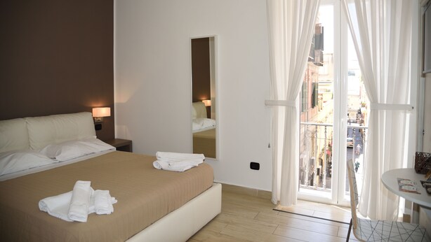Habitación de hotel con una cama grande, una mesita de noche con lámpara, un espejo y un balcón con cortinas.