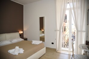 Habitación de hotel con una cama grande, una mesita de noche con lámpara, un espejo y un balcón con cortinas.