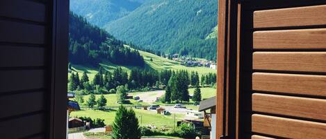 A view through an open door of a mountain landscape with a village, a road, and a mountain range.