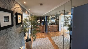 Un intérieur moderne avec un plancher en bois, une cloison en verre, des œuvres d’art encadrées au mur et un espace central agrémenté d’un meuble en bois et de plantes en pot.