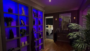 Un couloir avec une bibliothèque éclairée de lumière bleue, un tapis à motifs et une plante en pot.