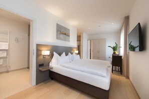A modern hotel room with a large bed, bedside tables, a flat-screen TV, and a potted plant. - Hotel Vitus Steyr (Steyr)