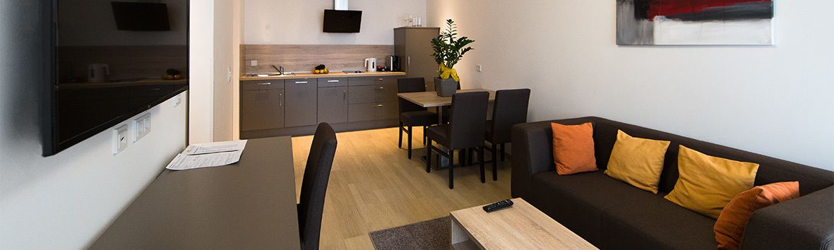 A modern living room with a sofa, a dining table, and a kitchen area in the background.
