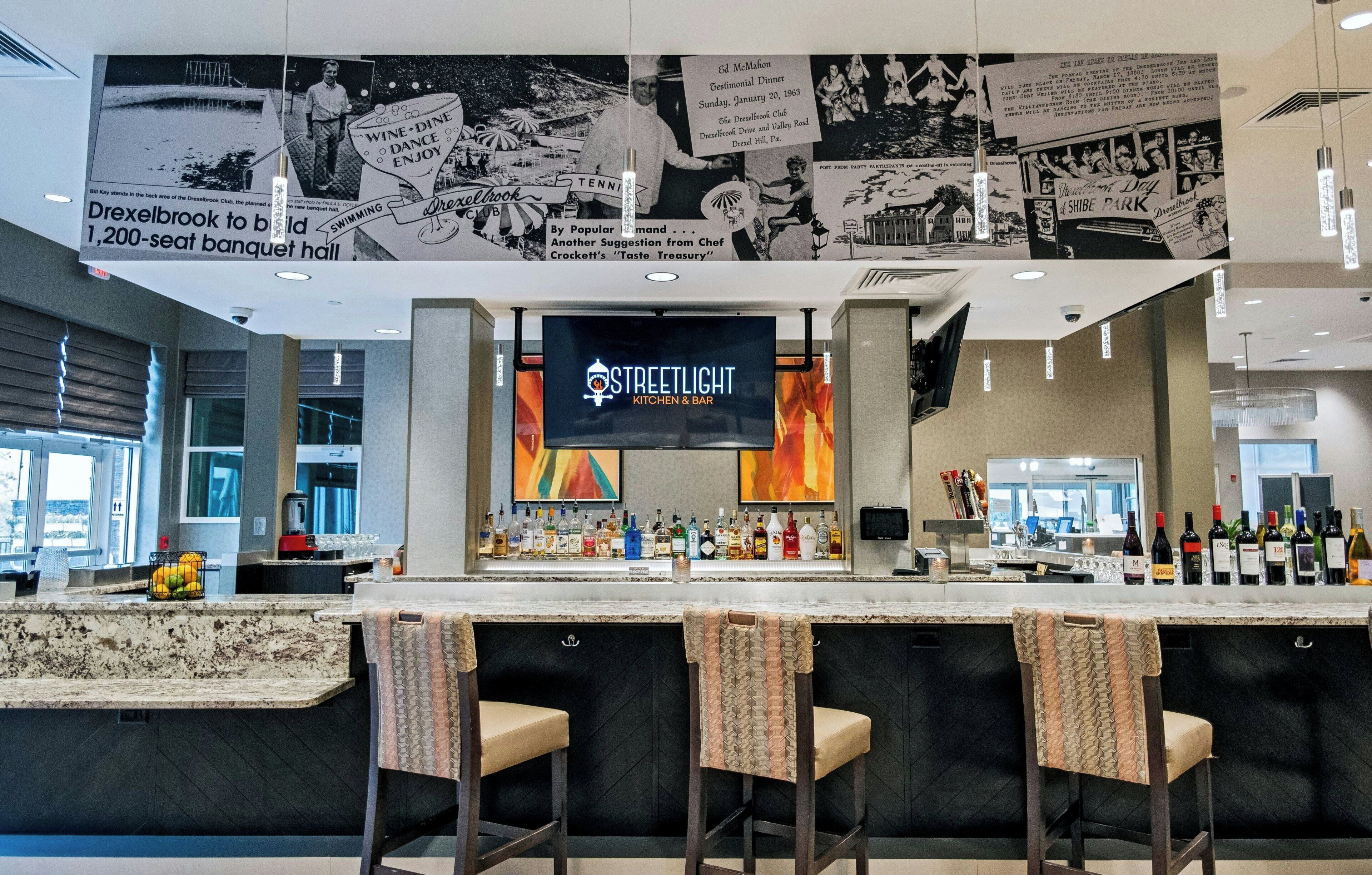 Zona de bar con barra, taburetes y una pantalla de televisión que muestra 'STREETLIGHT KITCHEN & BAR'.