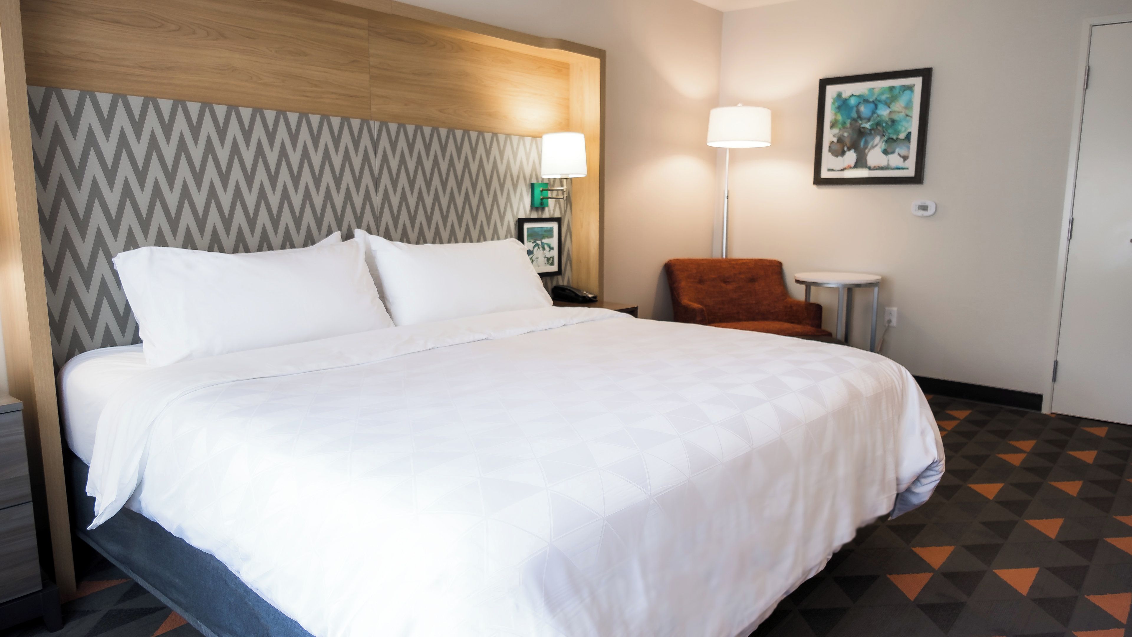Une chambre d’hôtel avec un grand lit, une chaise, une lampe et un tableau au mur.