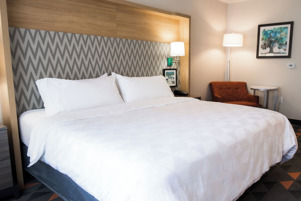 A hotel room with a large bed, a chair, a lamp, and a painting on the wall.