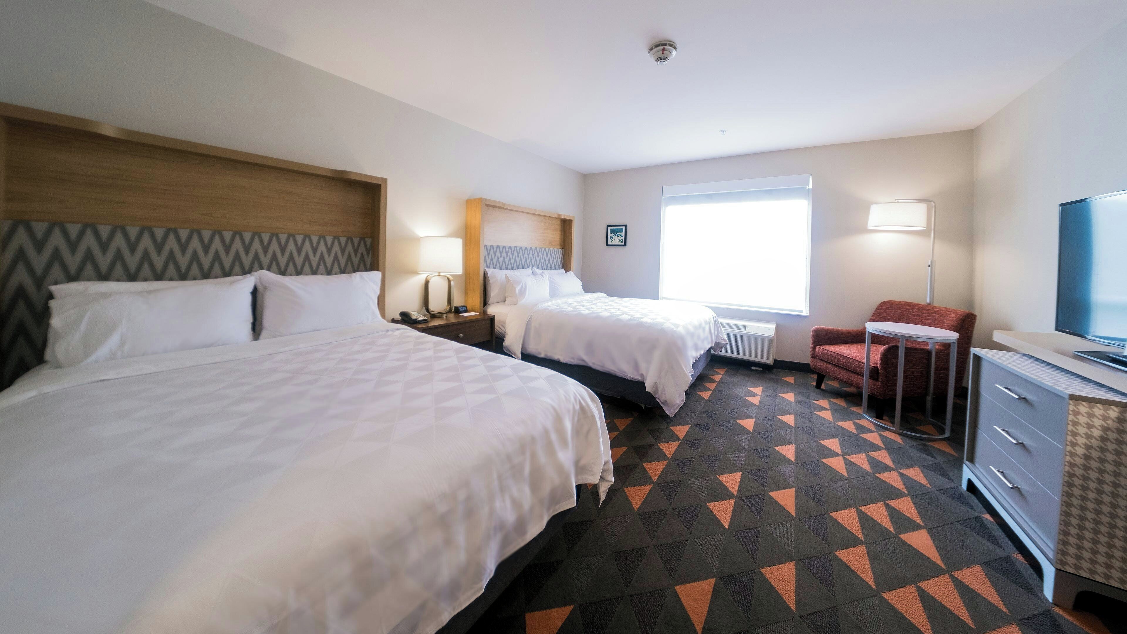 A hotel room with two beds, a desk with a television, a chair, and a window with blinds.