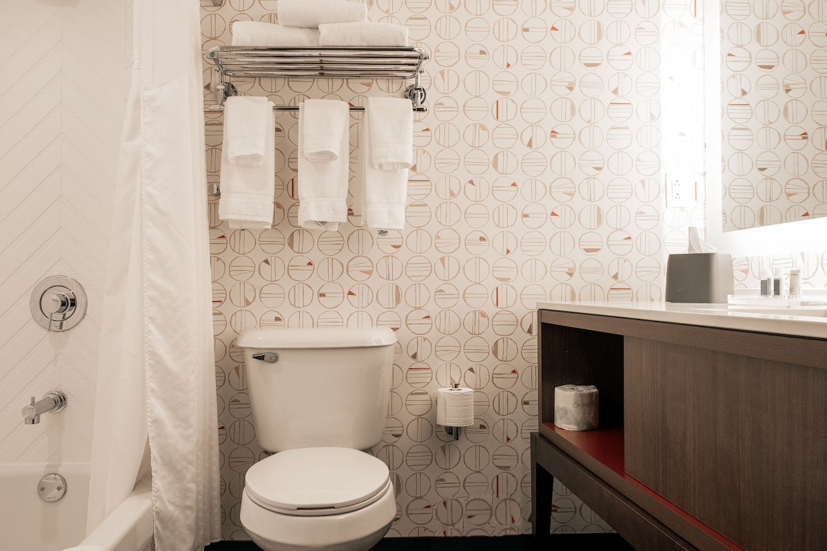 A bathroom with a toilet, a towel rack with multiple towels, a shower curtain, and a vanity with a mirror and toiletries.