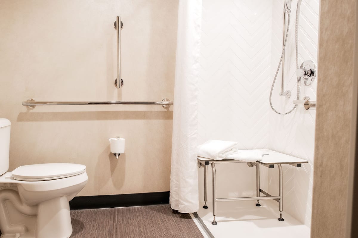 A small, clean bathroom with a toilet, a hand dryer, a towel rack, and a shower area.
