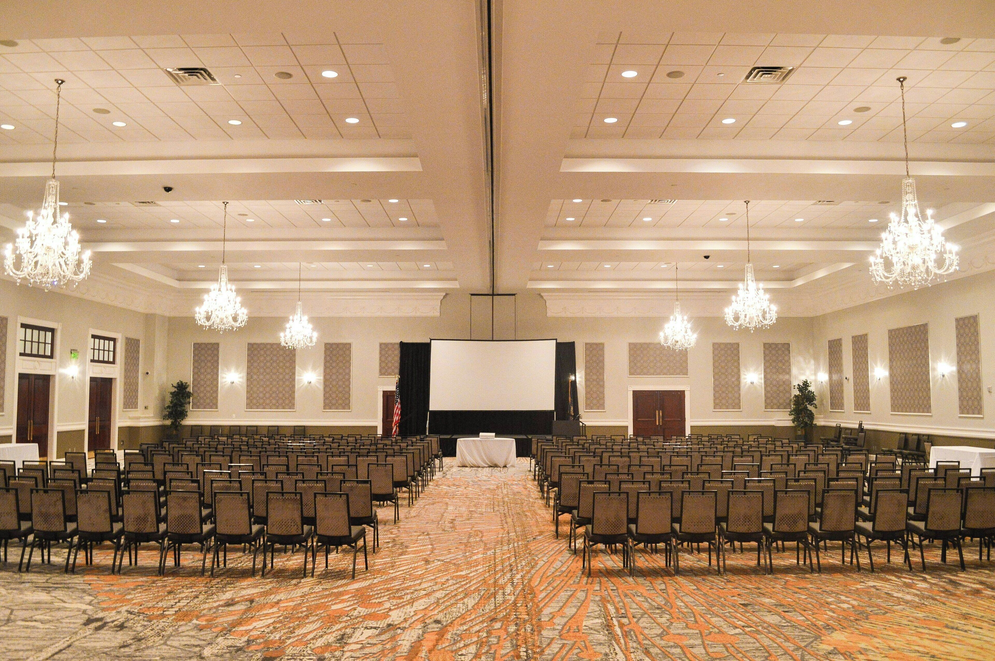 A conference room with rows of chairs, a large screen, and chandeliers.