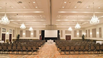 Een congreszaal met rijen stoelen, een groot scherm en kroonluchters.