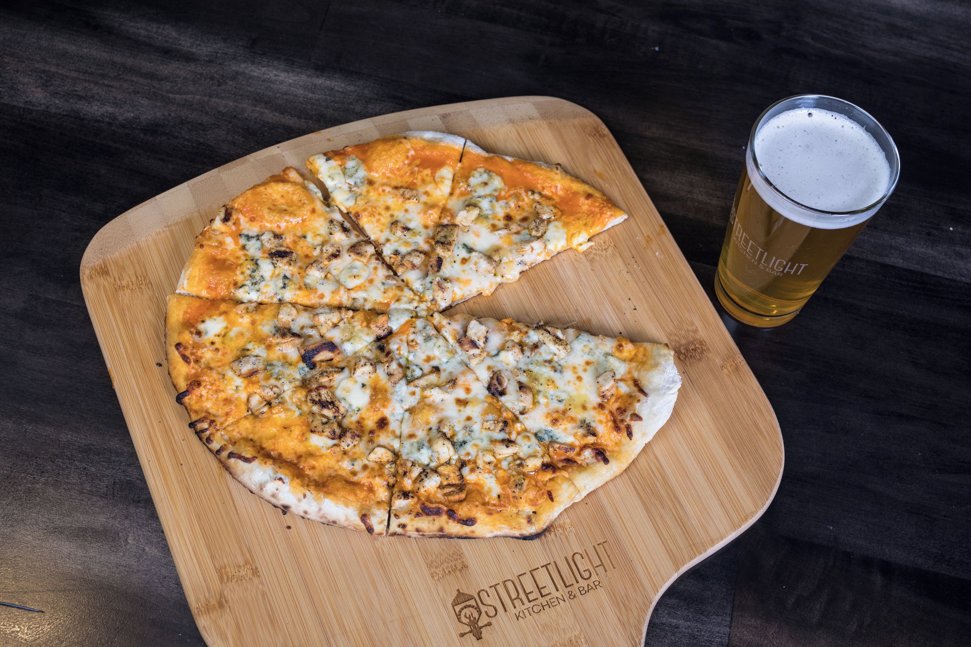 Una pizza su un tagliere di legno con un bicchiere di birra accanto.