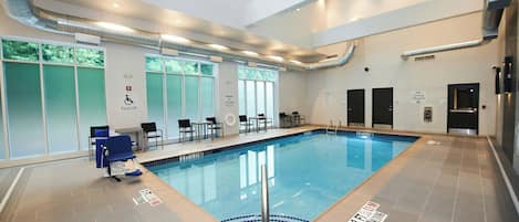 An indoor swimming pool with clear water, safety signs, and a pool lift chair.