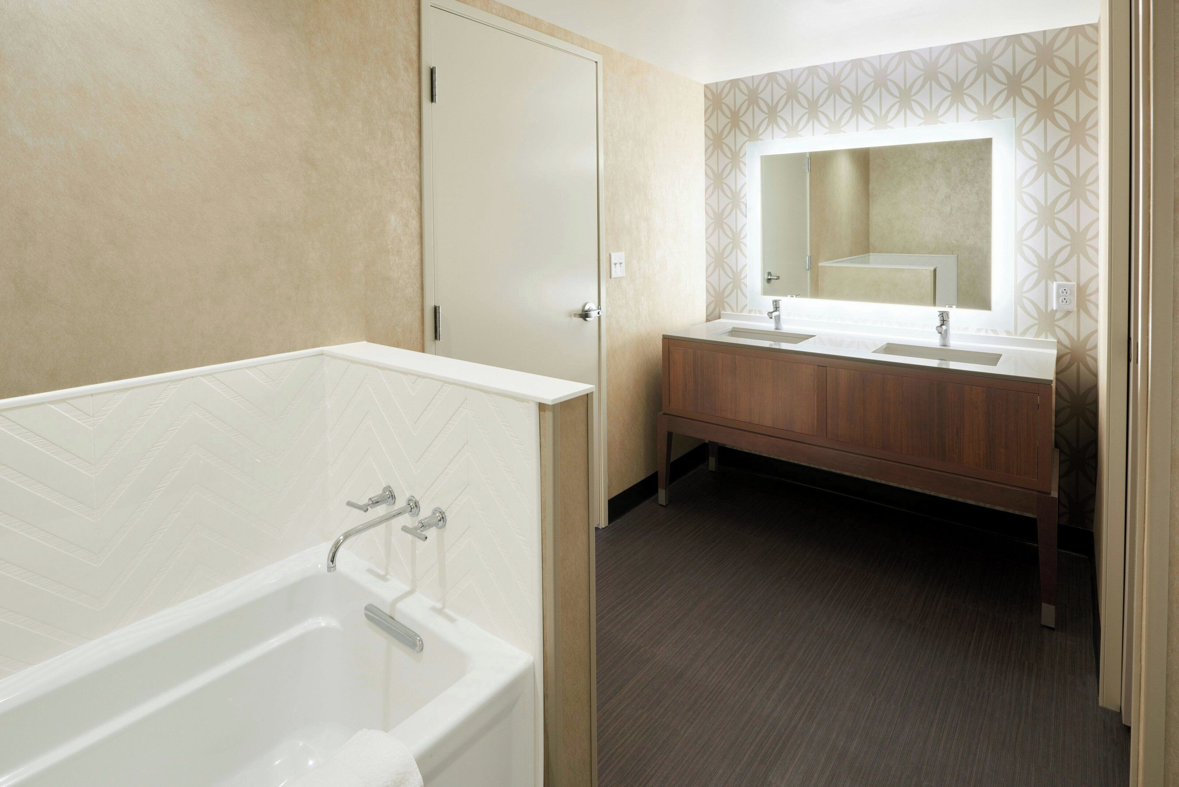 A bathroom with a bathtub, a double sink vanity, and a large mirror.