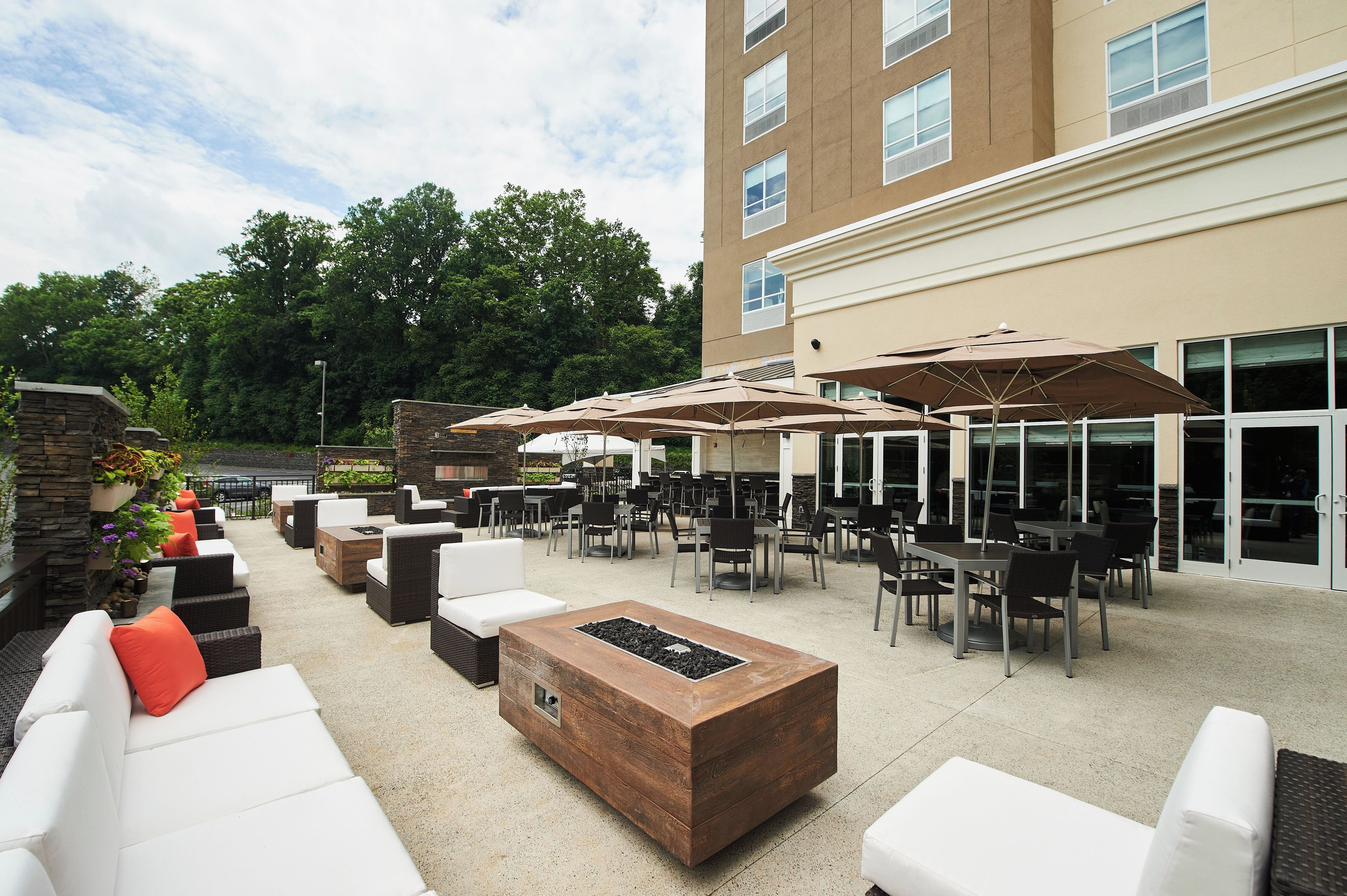 An outdoor patio area with multiple seating arrangements, including sofas and tables, and umbrellas providing shade.