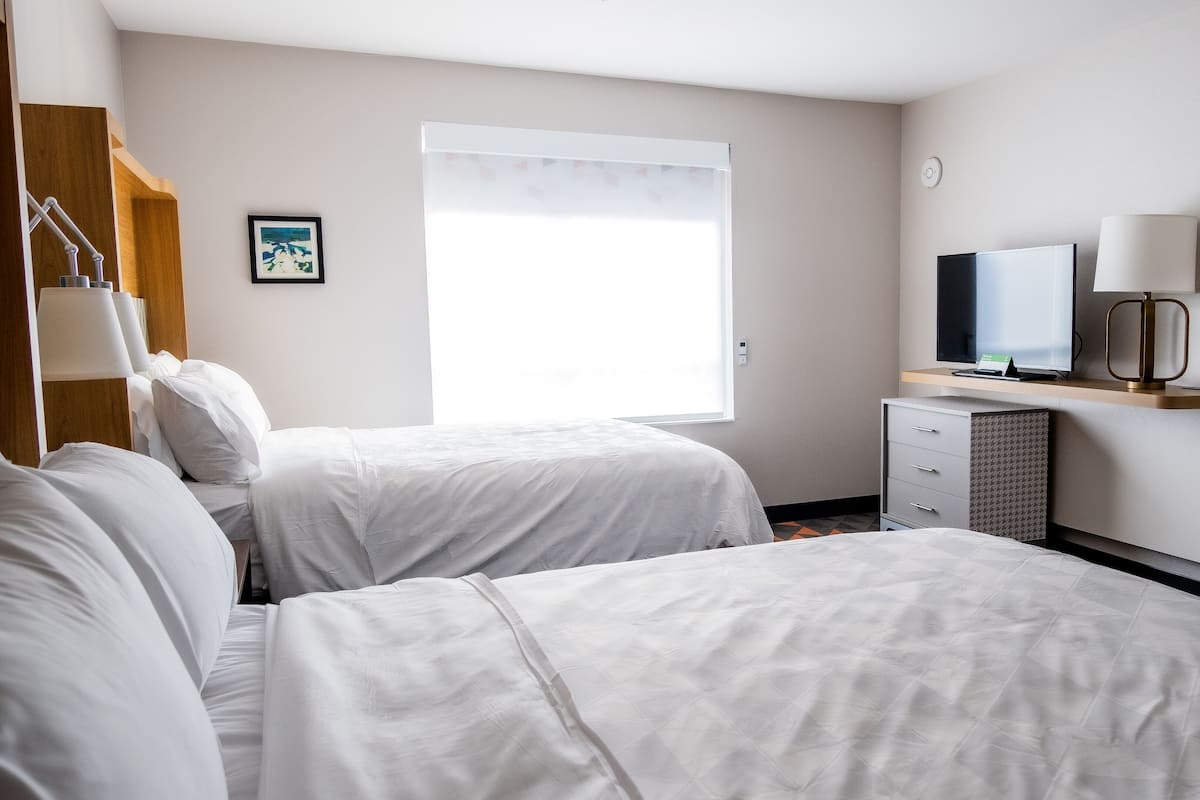 A hotel room with two beds, a desk with a computer, a television, and a window with blinds.