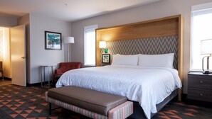 A hotel room with a large bed, a wooden headboard, a bench, a chair, and a desk with a lamp. - Holiday Inn & Suites Philadelphia W - Drexel Hill by IHG (Drexel Hill)