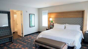 A hotel room with a large bed, a bench, a desk with a lamp, and a picture on the wall.
