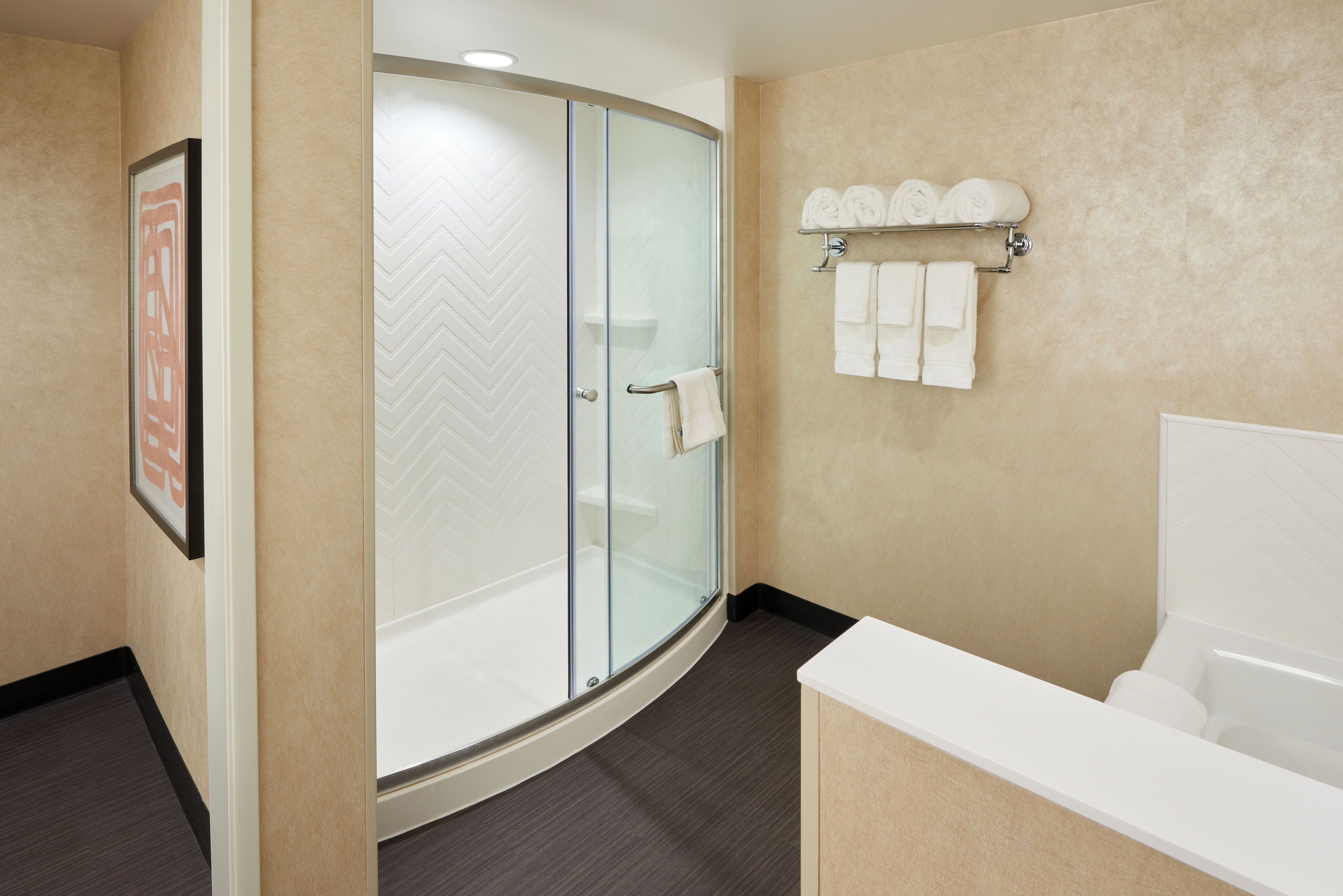 Une salle de bain moderne avec une douche à parois de verre, une baignoire blanche et un porte-serviettes où sont soigneusement pliées les serviettes.