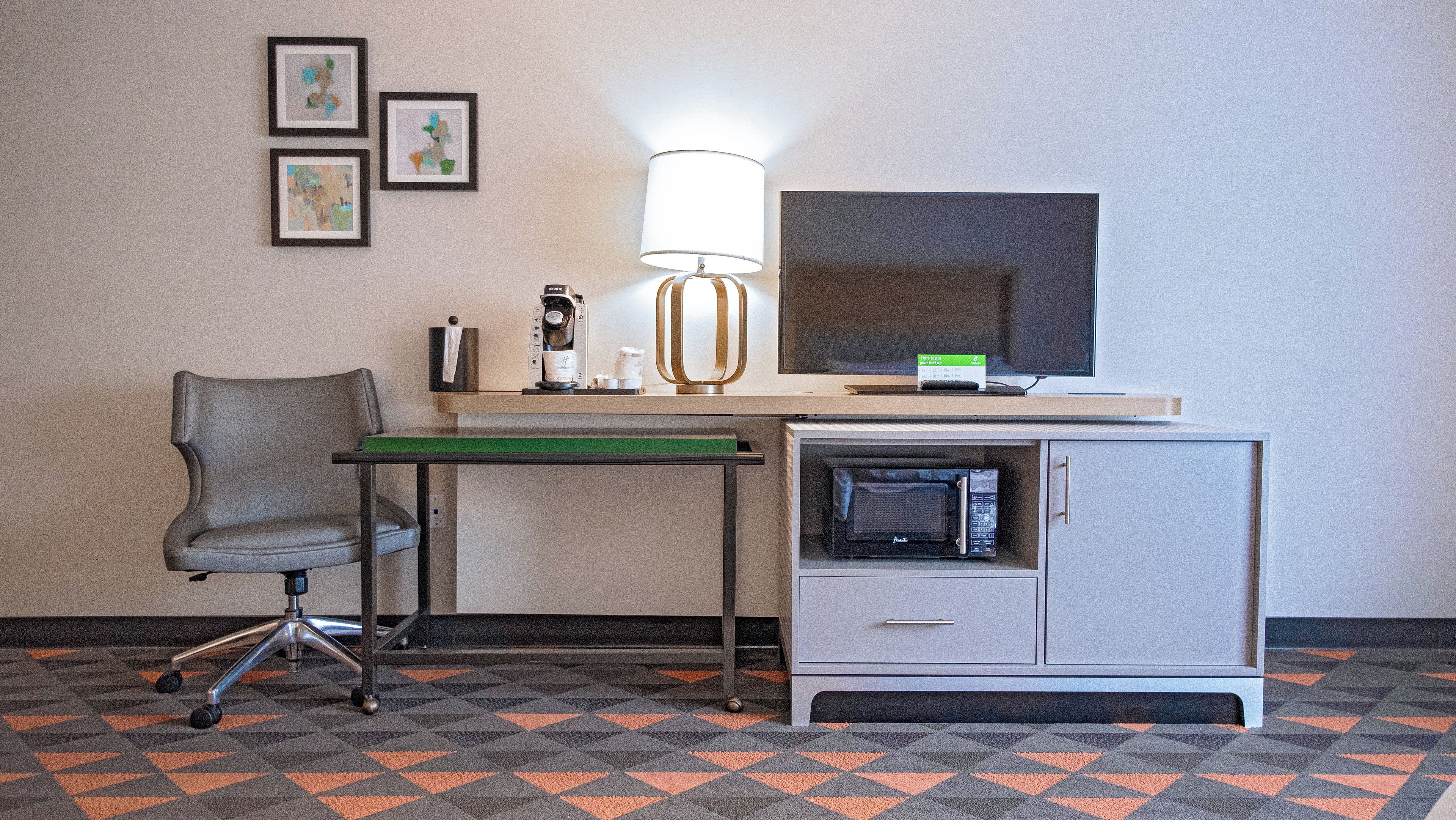 Une chambre d’hôtel équipée d’un bureau, d’une chaise, d’une lampe, d’une télévision, d’un four à micro-ondes et d’un petit placard.