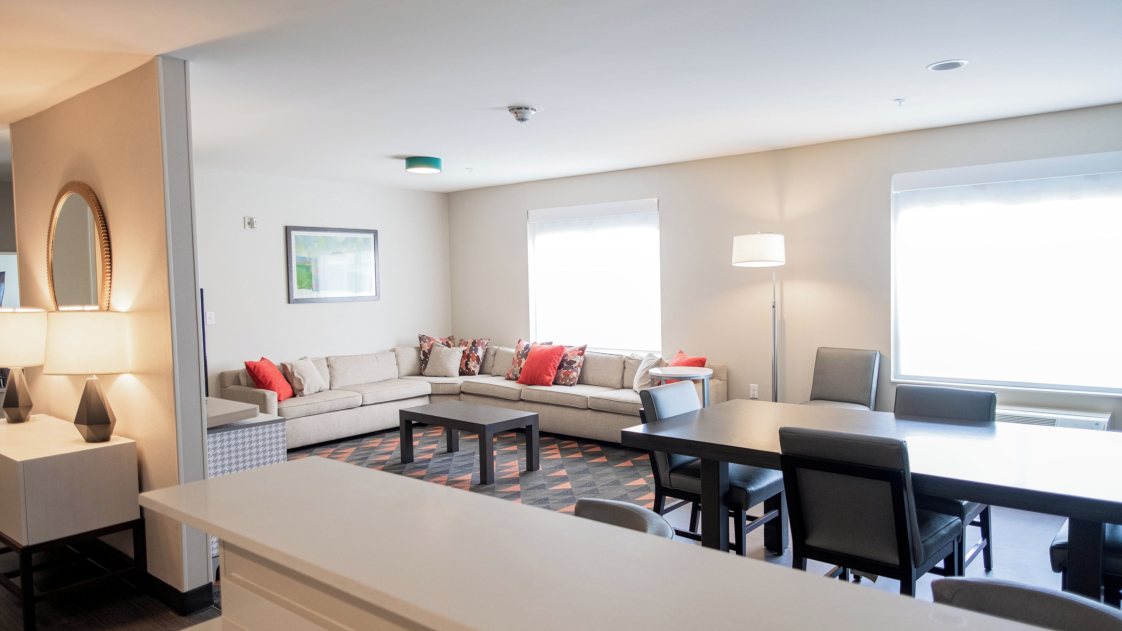 A modern living room with a sofa, a dining table, and chairs. There is a large window providing natural light.