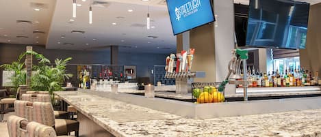 A bar area with a marble countertop, multiple seating options, a television screen, and a variety of bottles.