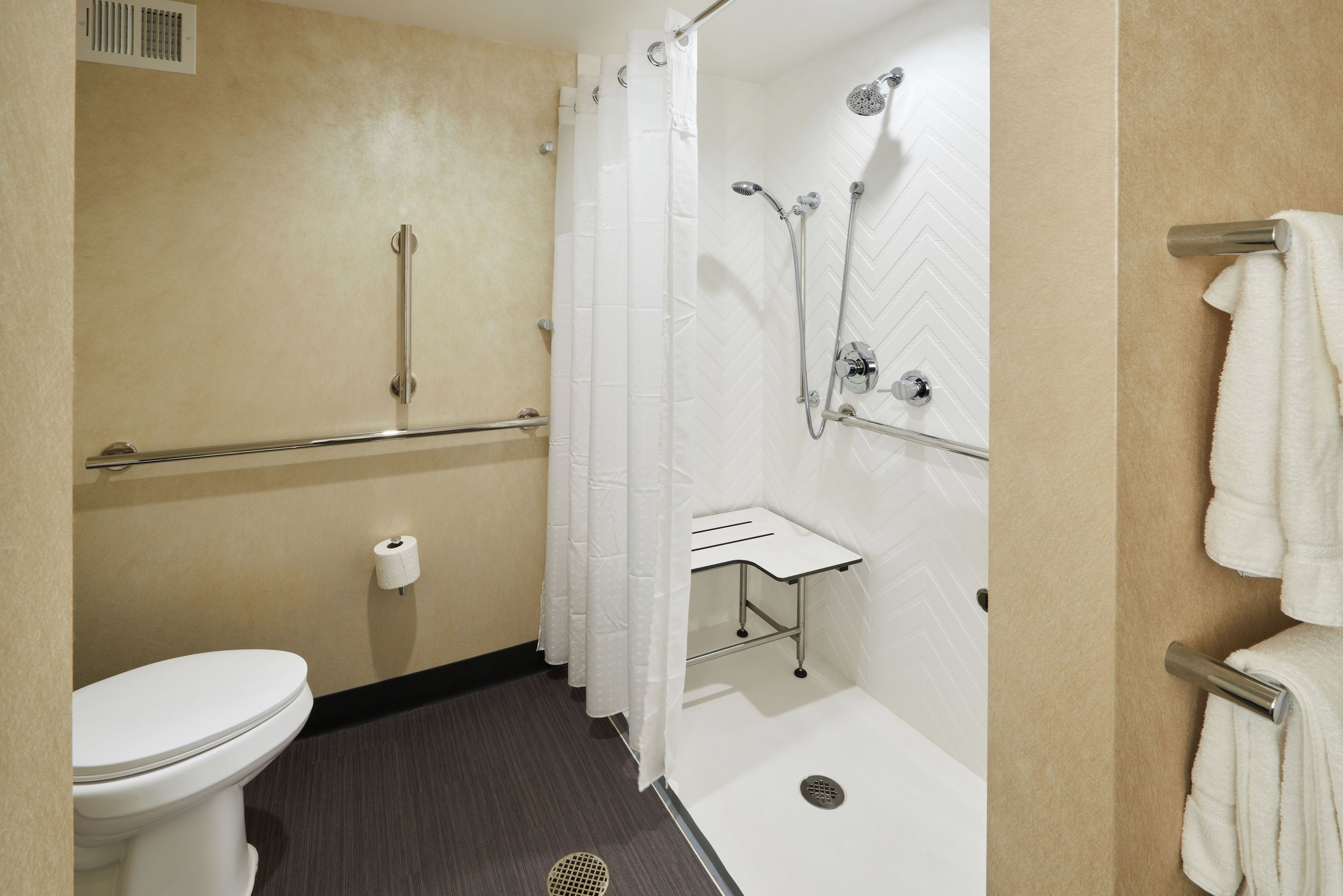Une salle de bain comprenant des toilettes, une douche avec un pommeau de douche amovible, un porte-serviettes et un support à papier toilette.