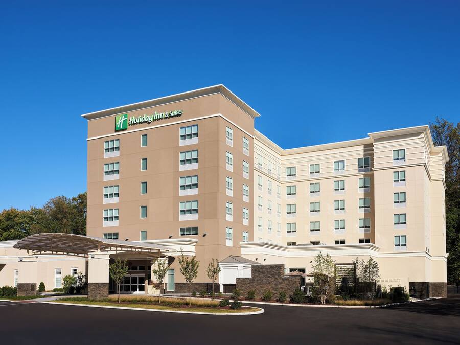Um hotel Holiday Inn & Suites com design moderno, apresentando um amplo estacionamento e fachada bem conservada.