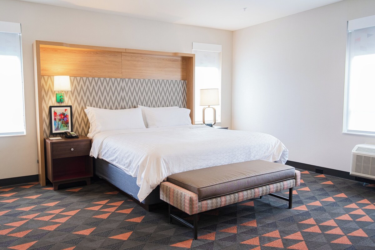 A hotel room with a bed, bedside tables, a bench, and a patterned carpet.