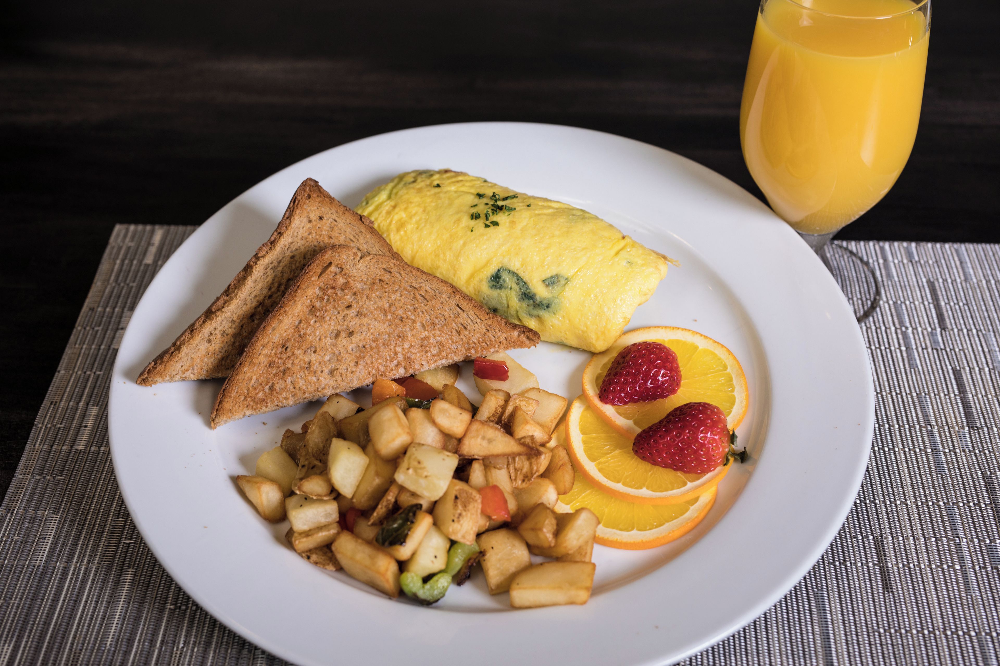 Un plato con tostadas, huevos revueltos, patatas y fruta sobre una alfombrilla.