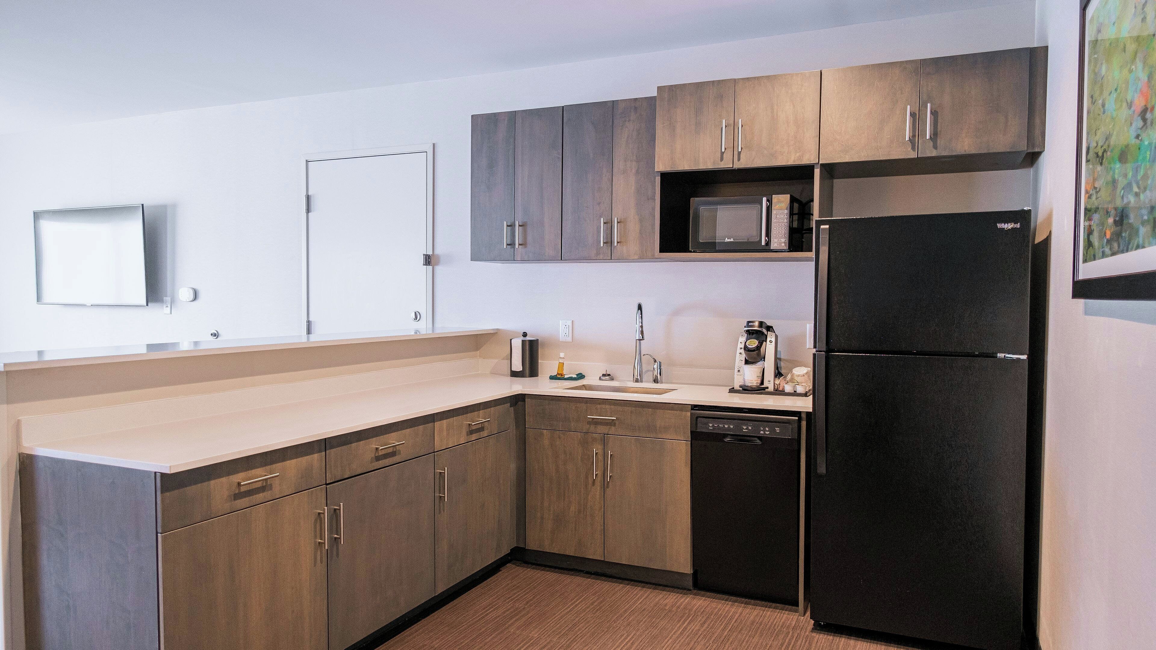 Una cocina moderna con armarios de madera, un refrigerador negro, un microondas y un lavavajillas.