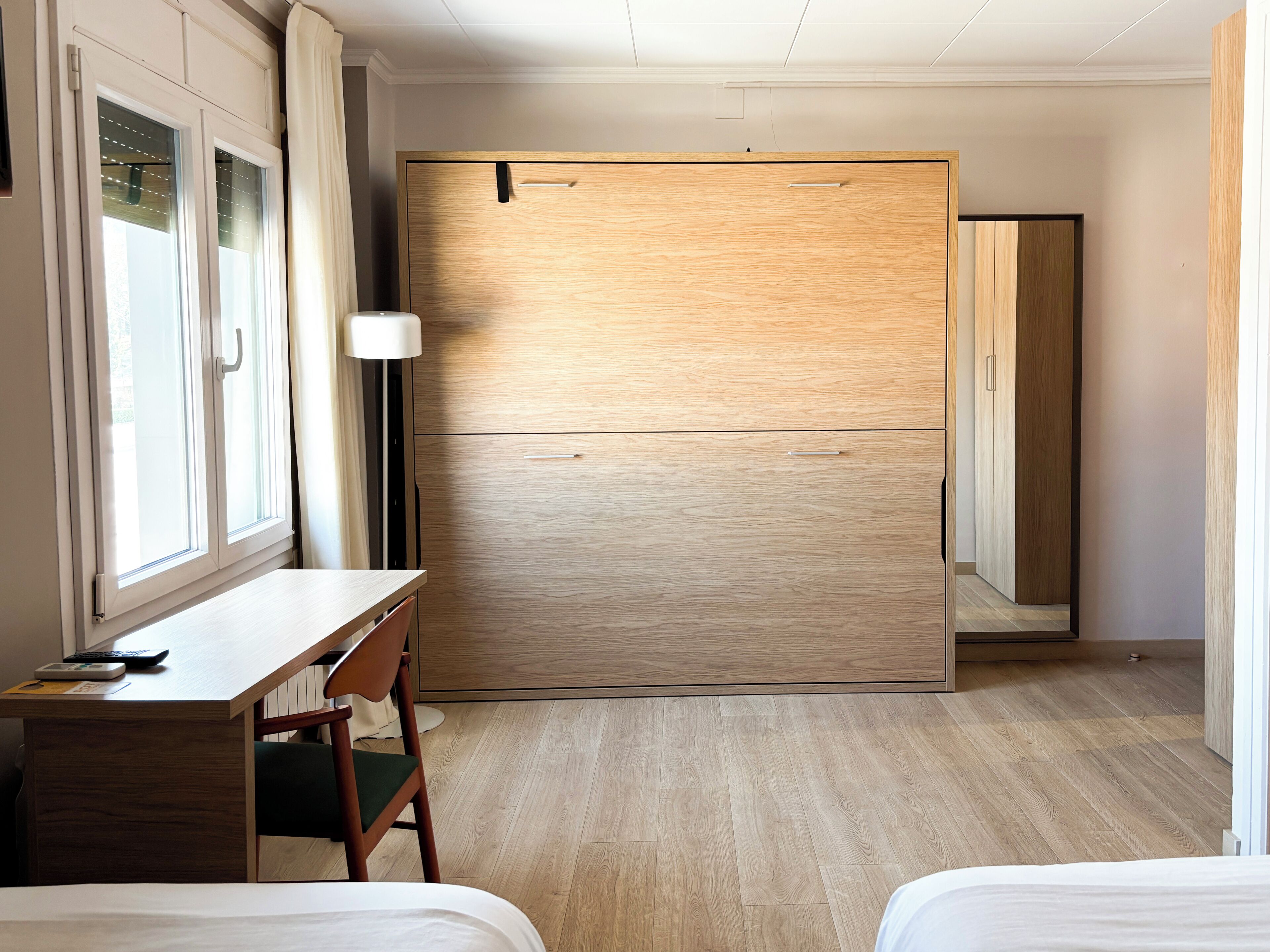 Een hotelkamer met een houten kast, een bureau met stoel, een bed en een vloerlamp.