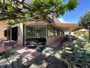 An outdoor seating area with tables and chairs, a covered walkway, and a building with a glass facade.