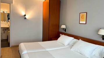 Habitación de hotel con una cama grande, un armario de madera, una mesita de noche con lámpara y un cuadro enmarcado en la pared.