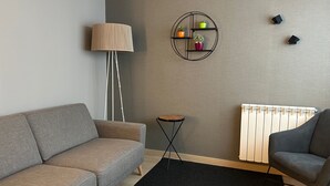 Una sala moderna con un sofá gris, un tapete negro, una lámpara de pie, una mesita auxiliar y un radiador.
