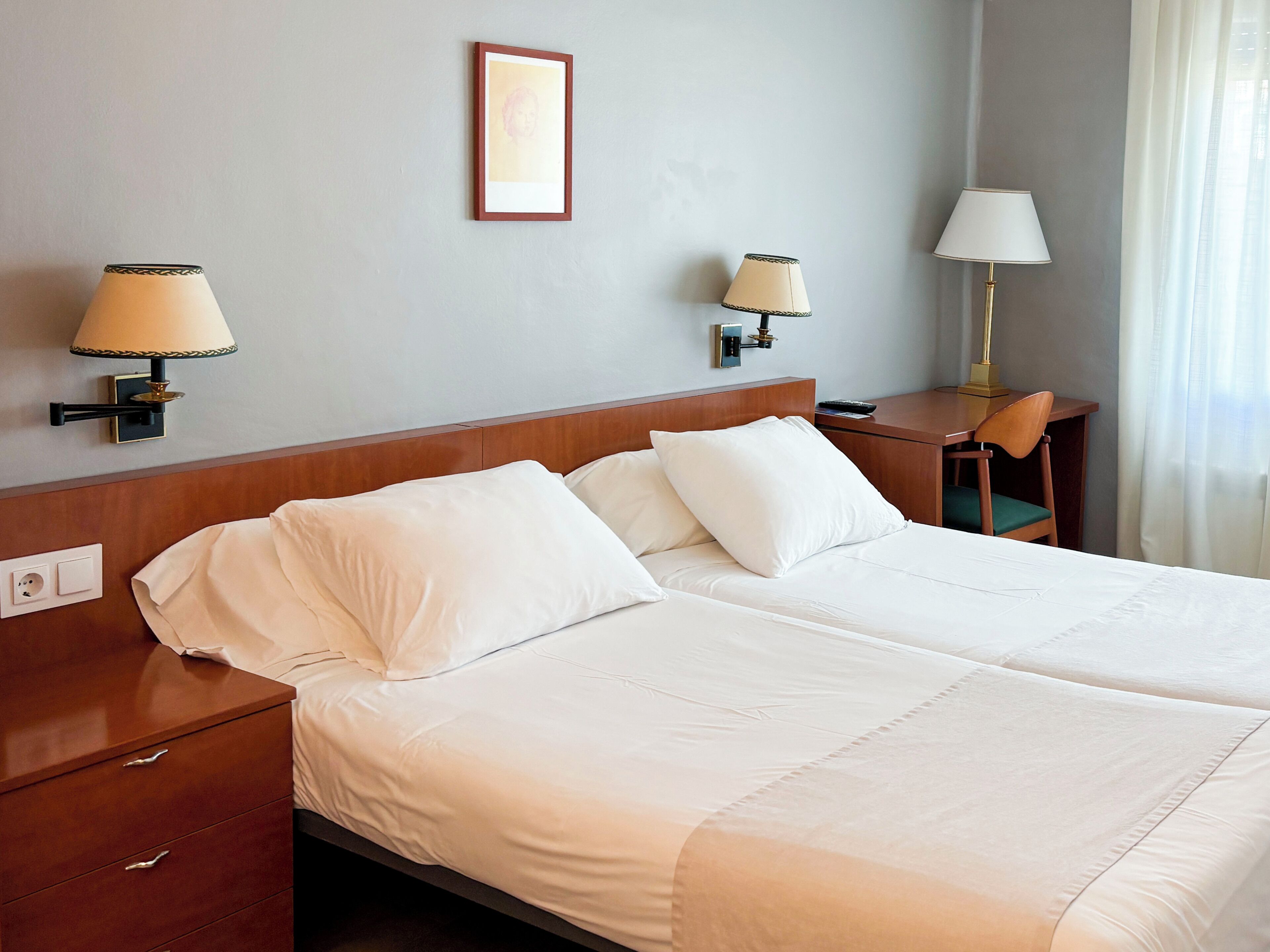 Habitación de hotel con dos camas, una mesita de noche, un escritorio y dos lámparas de pared.