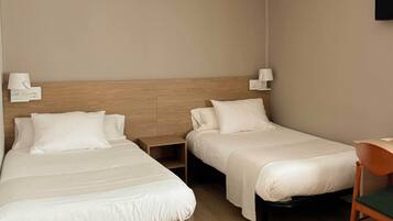 Quarto de hotel com duas camas, uma escrivaninha e uma cadeira.
