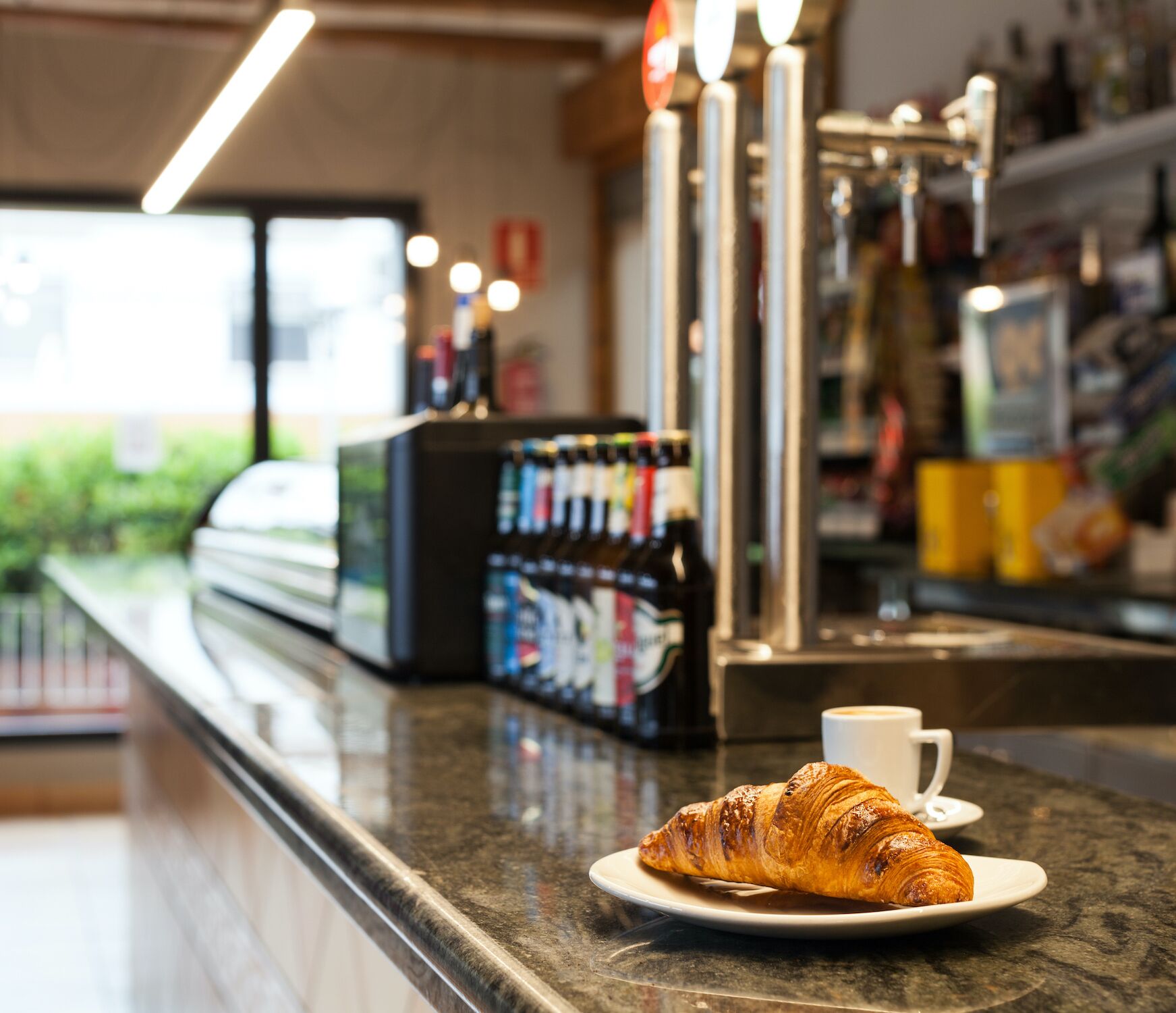 A croissant on a plate with a cup of coffee on a counter in a cafe.