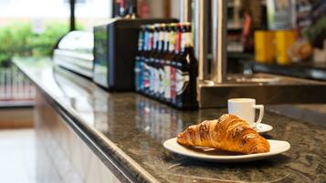 A croissant on a plate with a cup of coffee on a counter in a cafe.