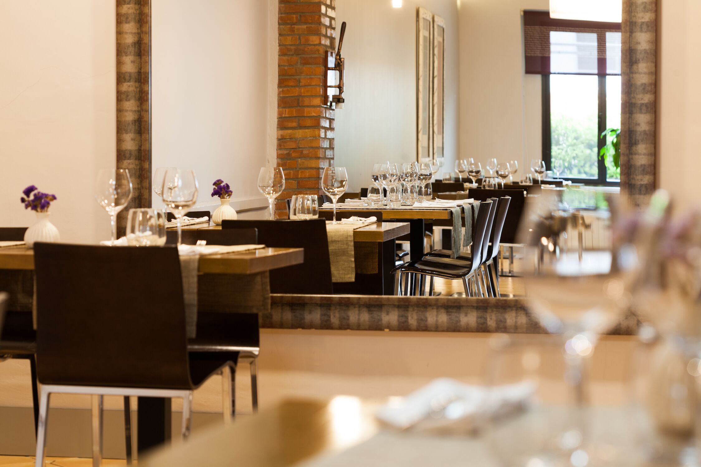 Een restaurant met meerdere tafels gedekt voor diners, met een bakstenen muur en grote ramen.